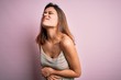 © Krakenimages.com - Young beautiful brunette girl wearing casual striped t-shirt over isolated pink background with hand on stomach because nausea, painful disease feeling unwell. Ache concept.