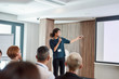© Svitlana - Dependable, professional partnership. Female speaker with laser pointer pointing at the screen while giving a talk on corporate business meeting