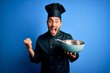 © Krakenimages.com - Young cooker man with beard wearing uniform using whisk and bowl over blue background screaming proud and celebrating victory and success very excited, cheering emotion
