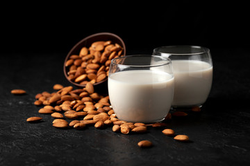 almond milk without sugar and lactose in glass with sprinkled nuts, vegetarian milk drink on a dark black table