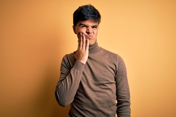 Poster - Young handsome man wearing casual turtleneck sweater over isolated yellow background touching mouth with hand with painful expression because of toothache or dental illness on teeth. Dentist