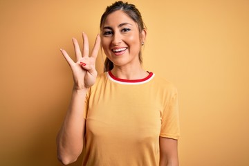 Wall Mural - Young beautiful athletic woman wearing casual t-shirt and ponytail over yellow background showing and pointing up with fingers number four while smiling confident and happy.