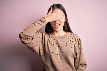 Poster - Young beautiful asian woman wearing fashion and elegant sweater over pink solated background smiling and laughing with hand on face covering eyes for surprise. Blind concept.