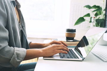 Closeup of female hands typing text on laptop keyboard.