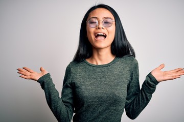 Wall Mural - Young beautiful chinese woman wearing glasses and t-shirt over isolated white background celebrating mad and crazy for success with arms raised and closed eyes screaming excited. Winner concept