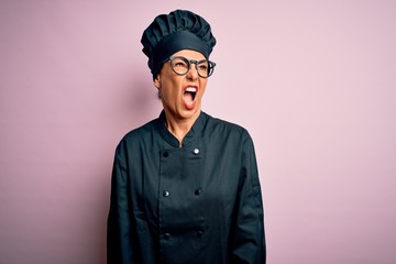 Poster - Middle age brunette chef woman wearing cooker uniform and hat over isolated pink background angry and mad screaming frustrated and furious, shouting with anger. Rage and aggressive concept.