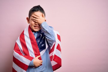 Wall Mural - Young little patriotic boy kid covered on united states of america flag on independence day stressed with hand on head, shocked with shame and surprise face, angry and frustrated. Fear and upset