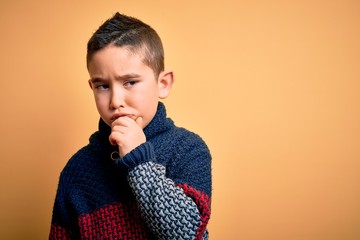 Wall Mural - Young little boy kid wearing winter sweater over yellow isolated background with hand on chin thinking about question, pensive expression. Smiling with thoughtful face. Doubt concept.