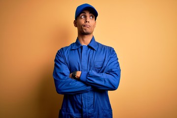 Wall Mural - Young african american mechanic man wearing blue uniform and cap over yellow background smiling looking to the side and staring away thinking.