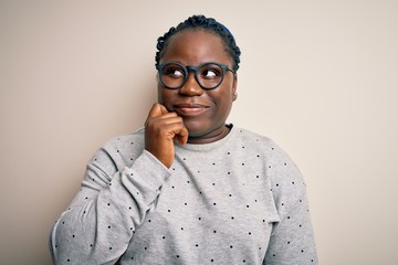 Sticker - Young african american plus size woman with braids wearing casual sweatshirt and glasses with hand on chin thinking about question, pensive expression. Smiling with thoughtful face. Doubt concept.