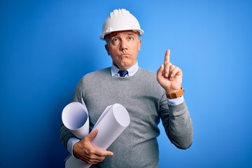 Poster - Middle age handsome grey-haired architect man wearing safety helmet holding blueprints Pointing up looking sad and upset, indicating direction with fingers, unhappy and depressed.