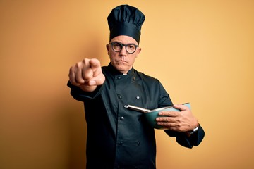 Canvas Print - Middle age handsome grey-haired chef man wearing cooker uniform and hat using whisk pointing with finger to the camera and to you, hand sign, positive and confident gesture from the front