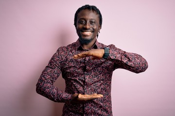 Poster - Young handsome african american man wearing casual shirt standing over pink background gesturing with hands showing big and large size sign, measure symbol. Smiling looking at the camera. Measuring