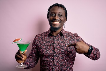 Poster - Young african american man drinking green cocktail. beverage over pink background with surprise face pointing finger to himself