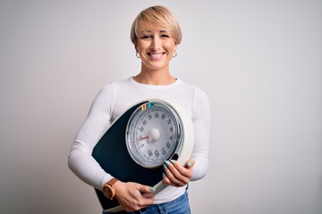 Sticker - Young blonde woman with short hair holding scale for healthy weight and lifestyle with a happy face standing and smiling with a confident smile showing teeth