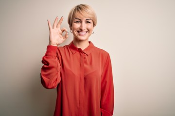 Sticker - Young beautiful business blonde woman with short hair standing over isolated background smiling positive doing ok sign with hand and fingers. Successful expression.