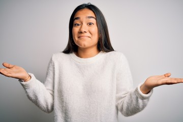 Canvas Print - Young beautiful asian woman wearing casual sweater standing over white background clueless and confused expression with arms and hands raised. Doubt concept.