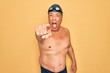 © Krakenimages.com - Middle age senior grey-haired swimmer man wearing swimsuit, cap and goggles pointing displeased and frustrated to the camera, angry and furious with you