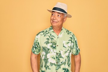 Canvas Print - Middle age senior grey-haired man wearing summer hat and floral shirt on beach vacation smiling looking to the side and staring away thinking.