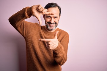 Middle age hoary man wearing casual brown sweater standing over isolated pink background smiling making frame with hands and fingers with happy face. Creativity and photography concept.