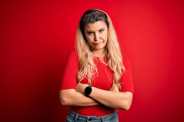 Sticker - Young beautiful blonde woman wearing casual t-shirt standing over isolated red background skeptic and nervous, disapproving expression on face with crossed arms. Negative person.