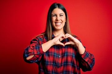 Canvas Print - Young beautiful woman wearing casual shirt over red background smiling in love doing heart symbol shape with hands. Romantic concept.