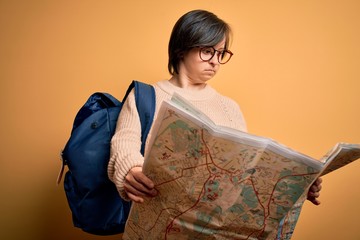 Sticker - Young down syndrome tourist woman wearing bag and looking at destination city map with a confident expression on smart face thinking serious