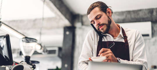 Portrait of handsome bearded barista man small business owner working and receive order from customer behind the counter bar in a cafe