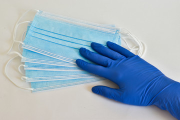 Hand in medical glove with thumb up, protective mask on a blue background. A typical three-layer surgical mask for covering the mouth and nose. The concept of protection against bacteria and viruses. 