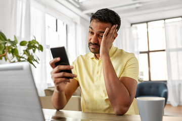 technology, remote job and business concept - stressed indian man with smartphone working at home office