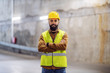 © Dusan Petkovic - Young smiling attractive construction worker in working clothes standing at construction site with arms crossed and looking at camera.