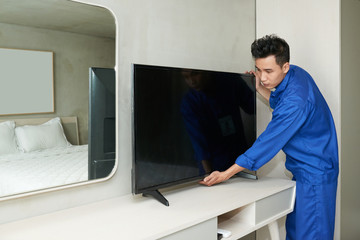 Sticker - Asian service worker in blue uniform putting television set on console in bedroom