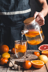 Wall Mural - A man pours citrus tea on a wooden table. Healthy drink, vintage style. Vegan, eco products.