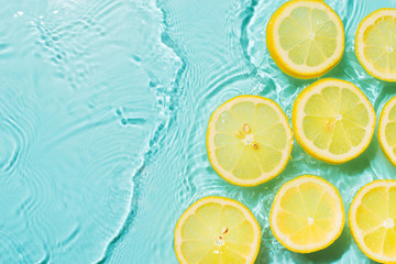 Wall Mural - Slice of lemon underwater or in water with splashing and droplet top view flat lay on blue background