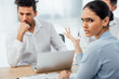 © LIGHTFIELD STUDIOS - Selective focus of skeptical mexican businesswoman looking at camera near african american colleague in office