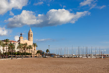 Beautiful View Of The Church Sant Bartomeu And Santa Tecla In Sitges With Boats On The Beach Under The Beautiful Sky.