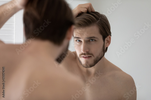Anxious young Caucasian man look in mirror in bathroom touch check head worried Tableau sur Toile