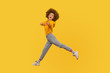 Hey you! Portrait of lively energetic curly-haired girl in urban style outfit walking through air in wide strides, pointing to camera and shouting message. studio shot isolated on yellow background