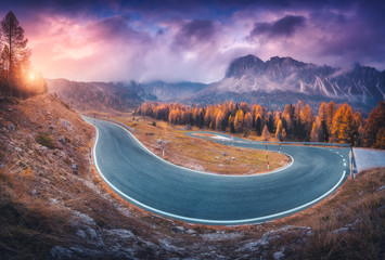 Wall Mural - Asphalt winding road in mountains at colorful sunset in autumn. Dramatic landscape with forest, beautiful highway, rocks, purple cloudy sky in fall. Roadway and trees with orange foliage. Travel