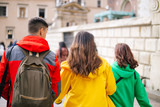 Fototapeta Londyn - Three young people tourists from behind in colored clothes as a traffic light (red, green yellow) walk, communicate, rest and travel