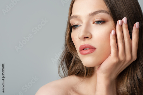 Beautiful young woman with healthy glow skin, long natural hair, nude colors makeup, manicure. Beauty, skincare, nail care advertising conception. Close up studio portrait. Copy, empty space for text