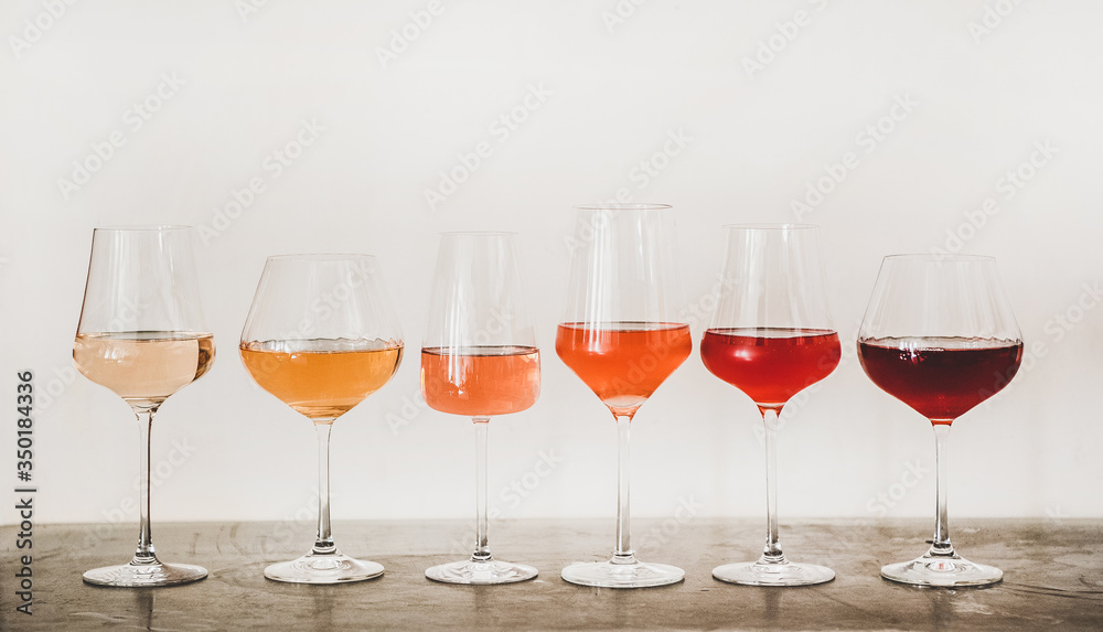 Various shades of Rose wine in stemmed glasses placed in line from light to dark colour on concrete table, white wall background behind. Wine bar, wine shop, wine tasting concept - obrazy, fototapety, plakaty 