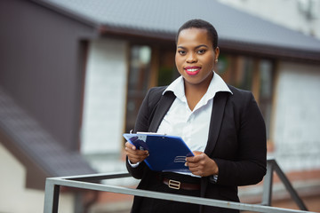 Paperwork. African-american businesswoman in office attire smiling, looks confident and happy, busy. Finance, business, equality and human rights concept. Beautiful young feme model, successful.