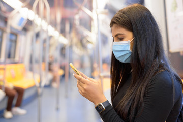 Poster - Young Indian woman with mask using phone and sitting with distance inside the train