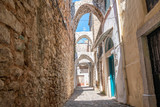 Fototapeta Na drzwi - A narrow alley with stone wall and houses with traditional geometric patterns on the facades and building arch. No people. An old motorbike standing in a doorway
