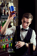 A Young Guy Working As A Bartender Behind A Bar Is Preparing Drinks For Customers.