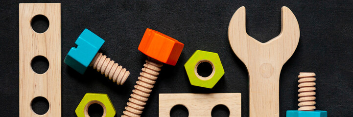 Set of colorful children's wooden toys. Construction kit with nuts and screws on dark black background. Interesting and fun game for boys and adults. Flat lay, top view, copy space for text. Banner