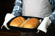 the cook holds a baking sheet with loaves of bread