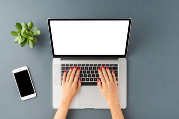 Overhead shot of woman’s hands using laptop with blank display on gray background. Modern workspace concept. Flat lay