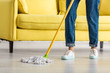 Cropped view of woman mopping floor with mop in living room